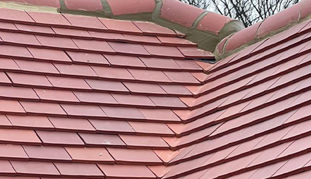 Newly installed red slate roof tiles along a ridge line.