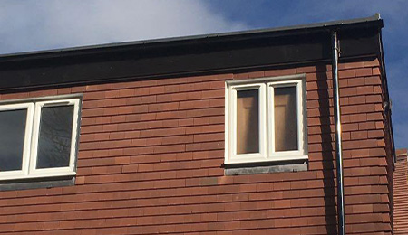 Two windows on a brown wooden facade with a black roof.