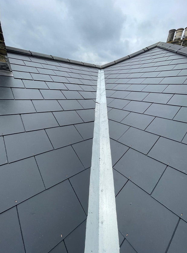 Newly installed slates on a roof with a metal ridge cap.